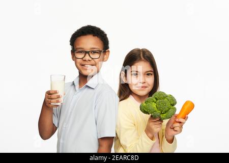 Latino-Amerikanisches Mädchen und afroamerikanischer Junge mit gesundem Essen und Milch. Gesunde Ernährung von Kindern Stockfoto