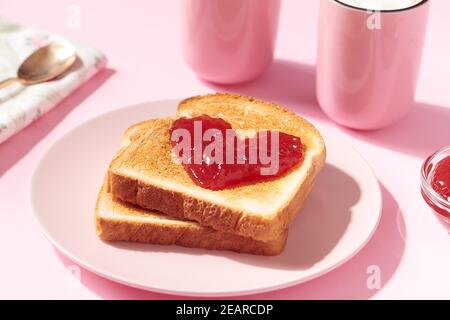 Toast mit herzförmiger Erdbeermarmelade darauf als ein Konzept für Liebe und Valentinstag Stockfoto