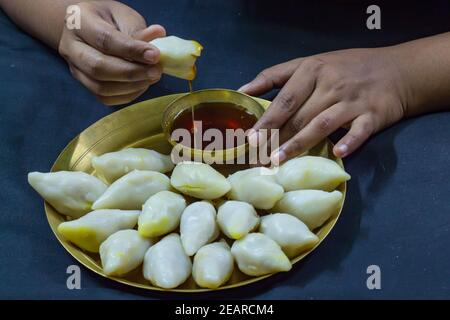 Köstliche bengalische Reismehl Kokosnussknödel serviert während bengali indian Festival von makar sankranti. Hände essen Knödel mit Dattelpalme Jaggery. Stockfoto
