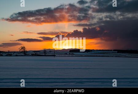 East Lothian, Schottland, Großbritannien, 10th. Februar 2021. UK Wetter: Ein feurig orangefarbener Himmel bei Sonnenuntergang über einer schneebedeckten Landschaft mit Blick auf die Umrisse der Pentland Hills in der Ferne Stockfoto