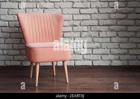 Moderner rosa weicher Stuhl gegen weiße Ziegelwand und braun Laminat im Fotostudio Stockfoto