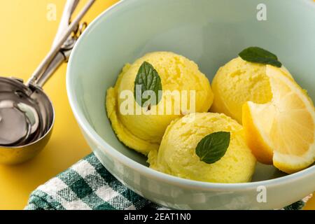 Zitroneneis Schaufel mit Minzblättern in Schale auf gelbem Hintergrund dekoriert. Nahaufnahme Stockfoto