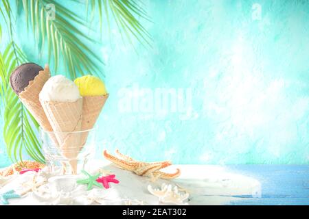 Sommer tropischen Urlaub am Meer Konzept. Drei Eis Waffelkegel mit verschiedenen Geschmacksrichtungen von Eis, auf Sand mit Muscheln und Seesterne, l Stockfoto