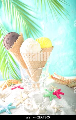 Sommer tropischen Urlaub am Meer Konzept. Drei Eis Waffelkegel mit verschiedenen Geschmacksrichtungen von Eis, auf Sand mit Muscheln und Seesterne, l Stockfoto