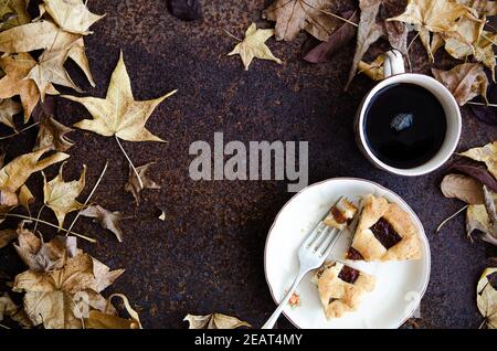 Stücke von Pastafrola auf einem weißen Teller mit einer Gabel und einer Tasse Tee, mit Baumblättern. Stockfoto