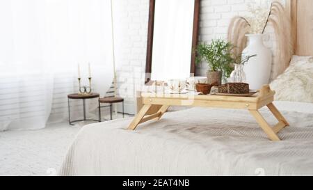 Das Frühstück wurde in der Nähe auf dem Zimmer serviert. Tassen auf einem Tablett mit Vase auf dem Bett. Selektiver Fokus. Skandinavischer Stil. Stockfoto