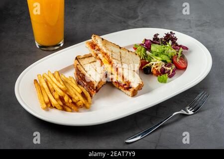 Toast mit Käse, Ei und türkischer Wurst serviert mit Salat und pommes auf weißem Teller Stockfoto