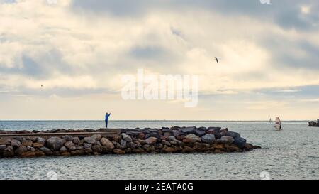 Ein Mann, der an einem bewölkten Tag mit seinem Handy vom Steinpier des Hafens von Fuengirola aus fotografiert. Stockfoto