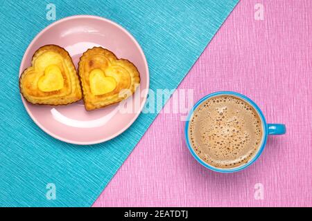 Morgenkaffee und herzförmige Cupcakes auf einer rosa-blauen Tischdecke. Romantisches Symbol. Valentinstag Frühstück in einem Café. Keramikbecher und -Teller, d Stockfoto