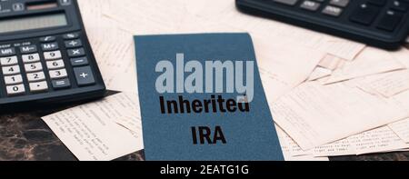 IRA erbte Text auf einem blauen Stück Papier auf einem Schreibtisch, neben schwarzen Taschenrechnern und vielen Schecks Stockfoto