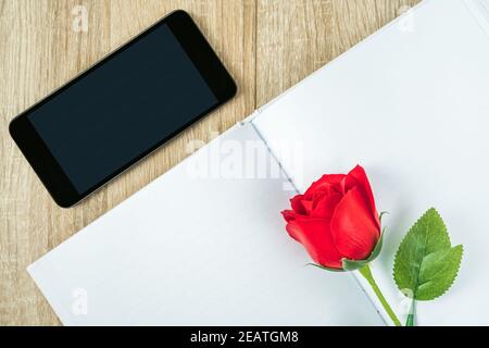 Rote Rosen auf leerem Notebook mit Smartphone Valentine Concept Stockfoto