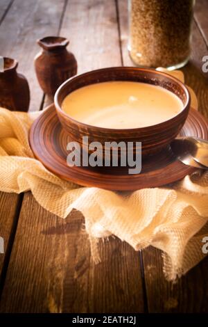 Suppe aus Buchweizen mit Milch in einer Keramikschale auf Rustikaler Tisch Stockfoto