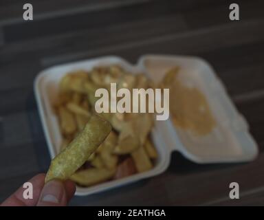 currywurst mit Pommes in eine Tasse. Traditionelle deutsche Küche zum Dip zu Corona Zeiten, konzentrieren sich auf Friese in der Hand Stockfoto