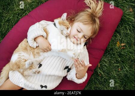 Kind mit Katze liegt auf einer Decke im Garten Stockfoto