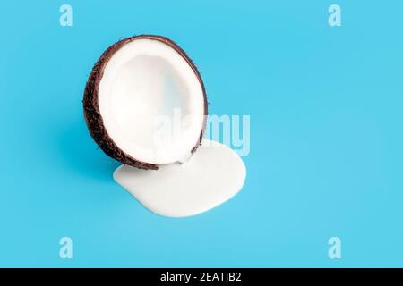 Kokosrahm oder Butter mit frischen Kokosnüssen auf blauem Hintergrund. Weißer Sahnesaft tropft aus Kokosnuss. Stockfoto