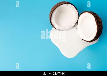 Kokosrahm oder Butter mit frischen Kokosnüssen auf blauem Hintergrund. Weißer Sahnesaft tropft aus Kokosnuss. Stockfoto