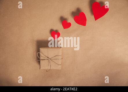 Hochwinkelansicht eines schlichten, umweltfreundlichen braunen Papiers Eingewickelt für Valentinstag Geschenk mit verschiedenen roten Herzen auf Brauner Papierhintergrund Kopierbereich Stockfoto
