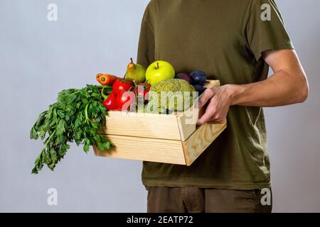 Mann in grünem T-Shirt mit Holzkiste voller Gemüse Stockfoto