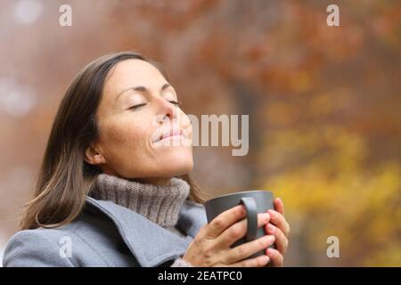 Entspannte Erwachsene Frau hält Kaffeetasse atmen im Herbst Stockfoto