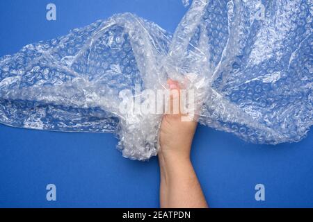 Weibliche Hand hält zerknittertes Stück Polyethylen mit Luftblasen Auf blauem Hintergrund Stockfoto