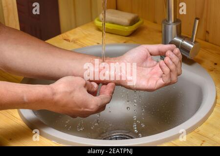 Ein Mann wäscht einen Abrieb auf seinem Arm unter Laufen Wasser Stockfoto