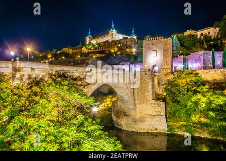 Nachtansicht der Alcantara Brücke über den Fluss Tajo mit Alcazar Burg im Hintergrund bei Toledo, Spanien Stockfoto