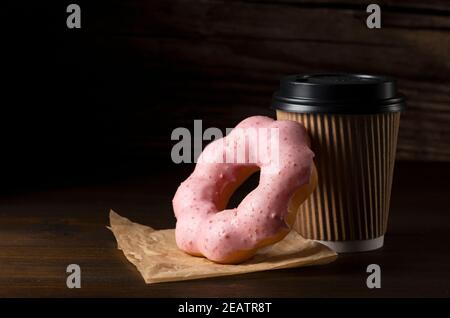 Heißer Kaffee in einer Papiertasse mit rosa Donuts auf Ein dunkler Holzhintergrund Stockfoto