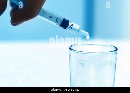 Ein Tropfen fällt aus dem Auslauf eines Reagenzrohrs In einen Glasbehälter in einem Wissenschaftslabor Stockfoto