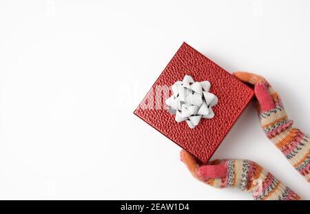 Weibliche Hände in gestrickten Fäustlingen halten eine rote Schachtel an Ein weißer Hintergrund Stockfoto