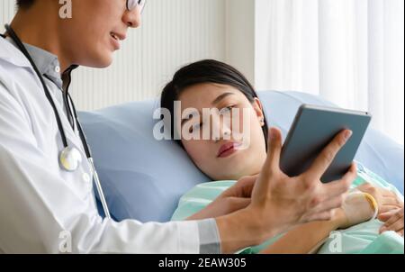 Patient liegt im Krankenhausbett Blick auf digitale Tablette mit Arzt sprechen ihre Gesundheit . Stockfoto