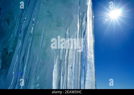 Lange Eiszapfen aus Eis gegen blauen Himmel und Sonne. Stockfoto