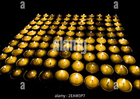 Ritualkerzen in breiten Kerzenleuchtern auf schwarzem Hintergrund. Tibetisches Kloster. Stockfoto