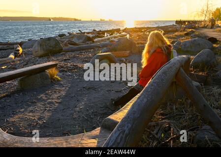 Frau auf der Treibholzbank, Sonnenuntergang, Ambleside Beach, West Vancouver, British Columbia, Kanada Stockfoto
