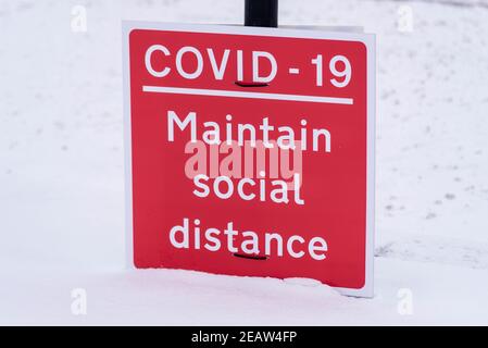 COVID 19, halten soziale Abstand Warnschild in Southend on Sea, Essex, Großbritannien, mit Schnee von Storm Darcy. Auf dem Boden Stockfoto