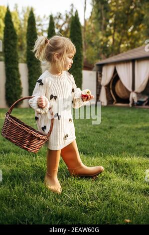 Kleines Mädchen mit Korb isst einen Apfel im Garten Stockfoto