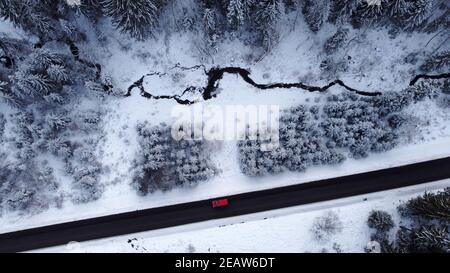 Luftdrohne Aufnahme einer Straße mit einem Auto fahren Im Winter durch den Wald Stockfoto