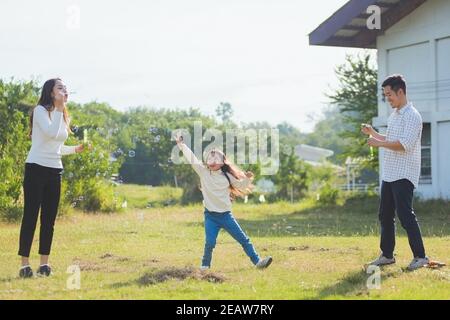 Asiatische Familie Mutter, Vater und kleines Mädchen mit Spaß zusammen spielen Blasen Seifenblasen im Park Stockfoto