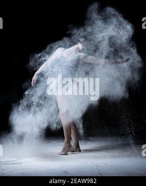 Frau mit einer Sportfigur tanzen in einer Wolke von Weißes Mehl auf schwarzem Hintergrund gestreut