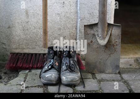 Alte abgenutzte Arbeitsstiefel mit einem Besen und Ein Spaten Stockfoto