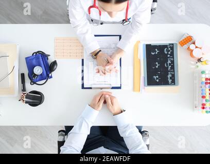 Arzt, der mit dem Patienten am Tisch in der Klinik kommuniziert, Draufsicht Stockfoto