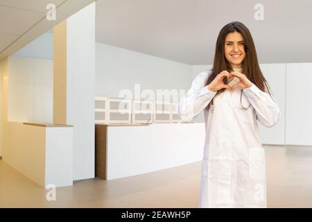 Schöne junge kaukasische weibliche Arzt oder Krankenschwester zeigt Herzform Mit Händen Stockfoto
