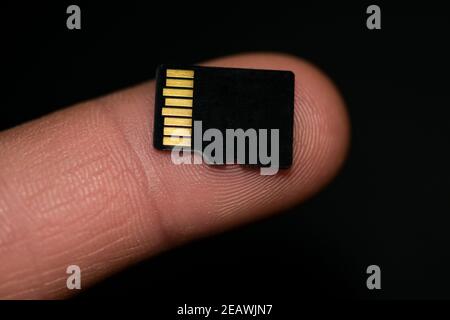 MicroSD-Karte auf menschlichen Finger über schwarzem Hintergrund, Hi-Tech-Daten Speichergeräte Stockfoto