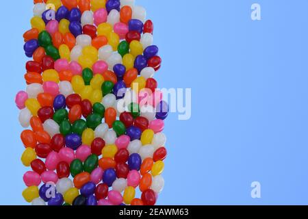 Mehrfarbige Jelly Bohnen in vertikaler Linie auf dem Spiegel mit der Reflexion des blauen Himmels Hintergrund. Draufsicht. Speicherplatz kopieren. 3-dimensional. Stockfoto