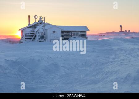 Anglikanische Kirche im arktischen Weiler Tuktoyaktuk im Winter, mit der fernen Frühwarnlinie im Hintergrund, Northwest Territories, Kanada. Stockfoto