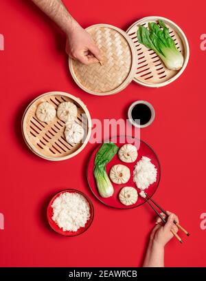 Chinesischer Esstisch mit gedünsteten Baozi-Knödeln aus Schweinefleisch, pak Choi und Reis, isoliert auf rotem Hintergrund. Draufsicht mit chinesischen Xiao Long Bao Buns. Stockfoto