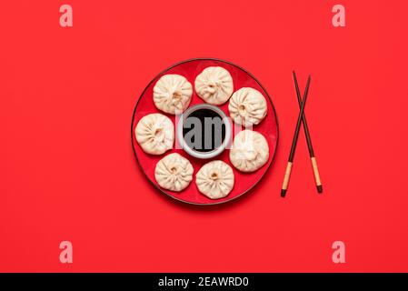 Bao Knödel auf rotem Teller mit chinesischer Sauce, isoliert auf rotem Hintergrund. Gedämpftes Schweinefleisch Baozi, hausgemachtes xiao Long bao, Draufsicht. Dampfbrötchen. Stockfoto