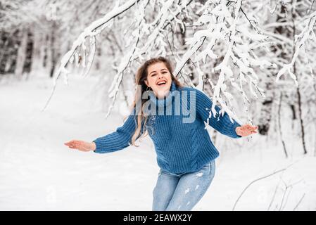 Schöne Winter Mädchen in einem blauen gemütlichen Strickpullover spielen Mit Schnee Stockfoto