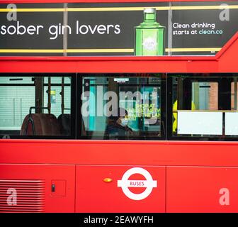 Roter Londoner Bus mit einer alleinreisenden Beifahrerin in Gesichtsmaske sitzend. Werbung für Gin-Flasche auf der Außenseite Stockfoto