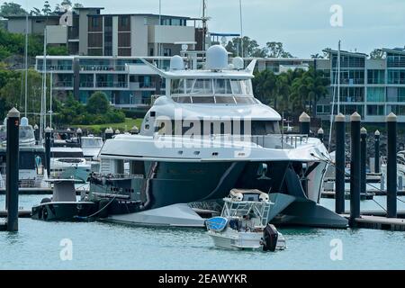 Airlie Beach, Queensland, Australien - Februar 2021: Eine große Luxusyacht liegt am Yachthafen mit einem kleinen Motorboot im Vordergrund Stockfoto