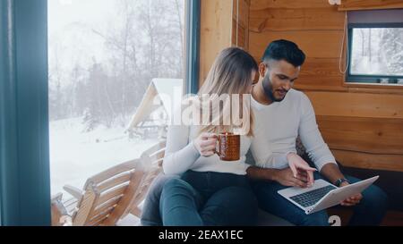 Glückliches junges Paar genießen Winterurlaub. Surfen in sozialen Medien auf dem Laptop und trinken heiße Getränke. Hochwertige Fotos Stockfoto